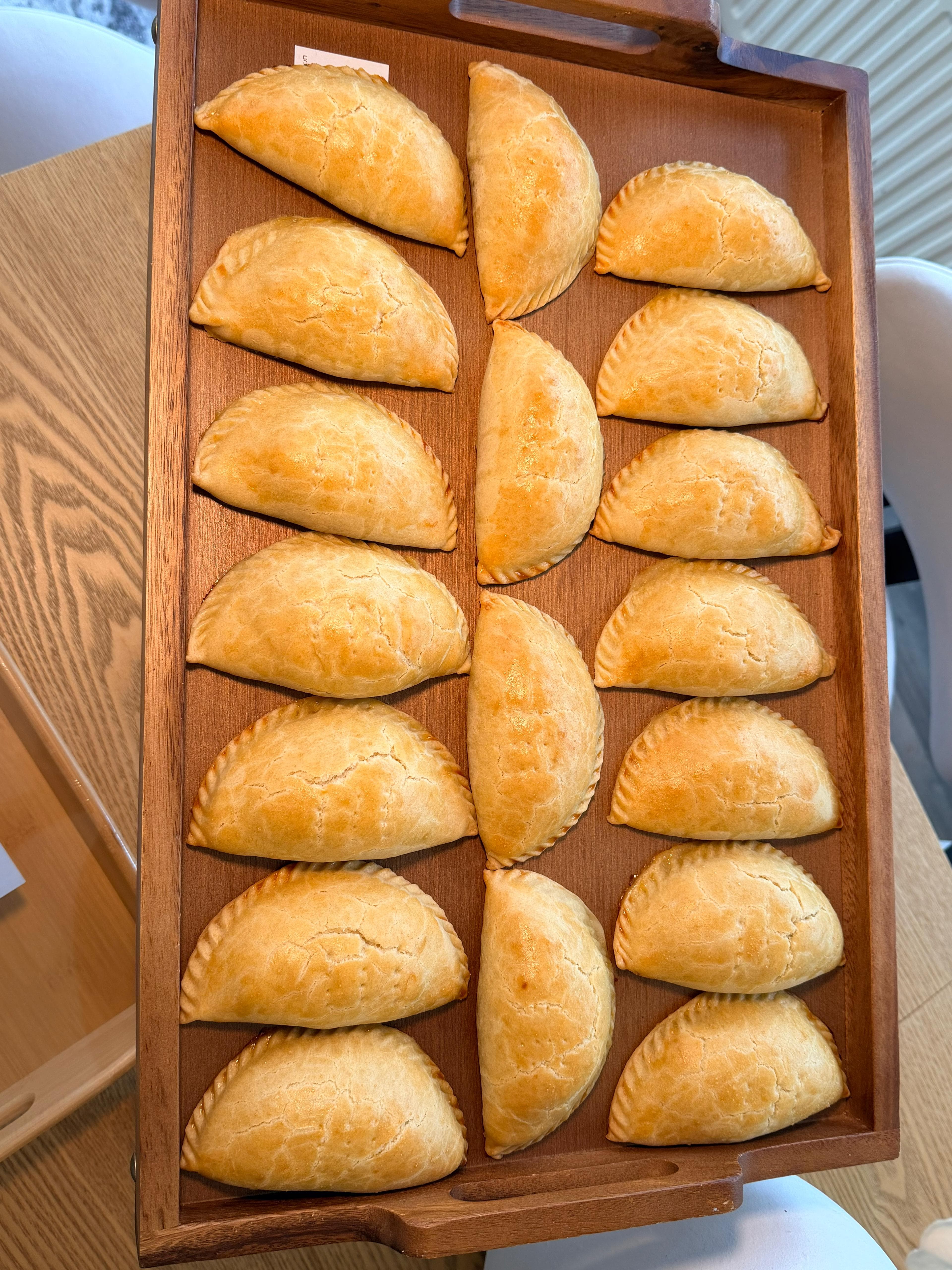 Hand-folded chicken pies arranged on a wooden tray
